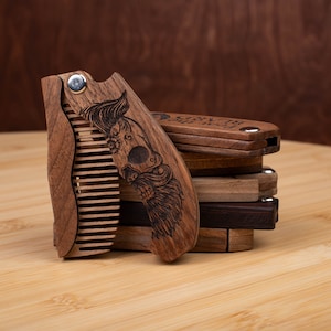 May include: A wooden comb with a skull and beard design. The comb is folded and has a metal hinge. The comb is made of dark wood and has a natural finish. The comb is part of a set of wooden combs.