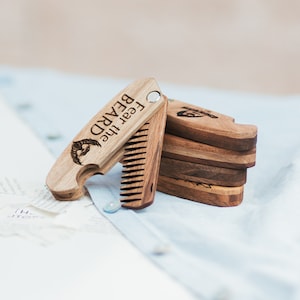 Könnte beinhalten: Ein Holzbartkamm mit integriertem Flaschenöffner. Der Kamm ist mit den Worten "Fear the Beard" graviert.