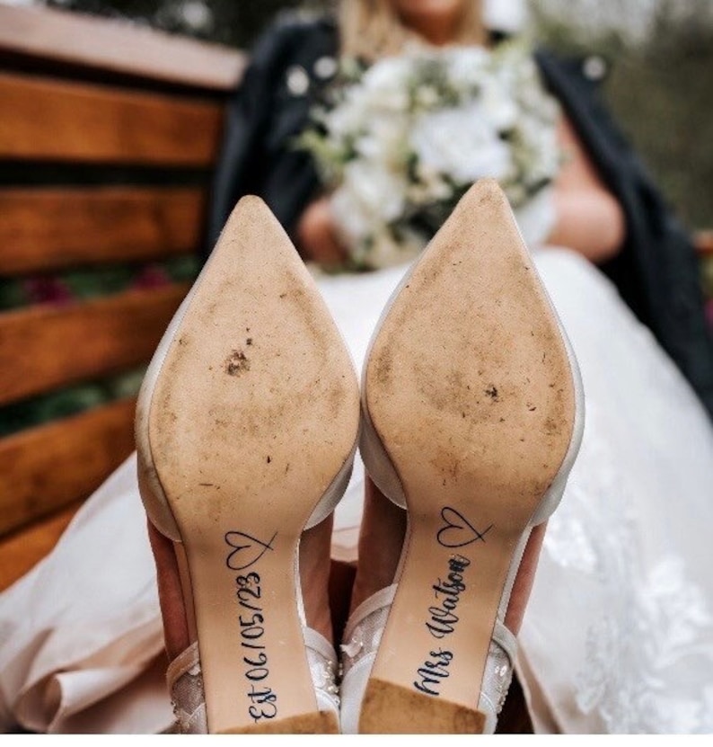 May include: A pair of white bridal shoes with the text "Est 06.10.5123" and "Mrs. Watson" written on the soles.