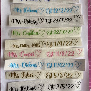May include: A collection of white labels with black text and hearts. Each label has a name followed by "Est" and a date. The dates are in the format MM/DD/YY. The names include Mrs. Champion, Mrs. Patton, Mrs. Holman, Mrs. Vickery, Mrs. Coghlan, Mrs. Dilley-Wills, Mrs. Cooper, Mrs. Dickens, Mrs. Fisher, Mrs. Holland, and Mrs. Crichton.