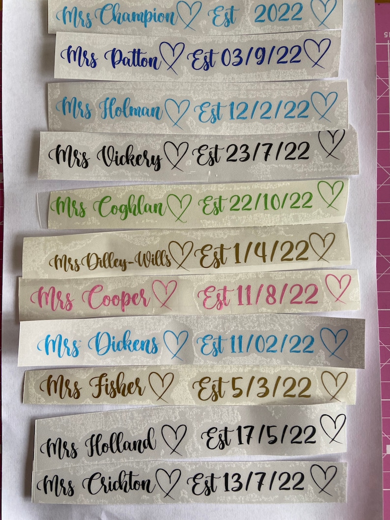 May include: A collection of white labels with black text and hearts. Each label has a name followed by "Est" and a date. The dates are in the format MM/DD/YY. The names include Mrs. Champion, Mrs. Patton, Mrs. Holman, Mrs. Vickery, Mrs. Coghlan, Mrs. Dilley-Wills, Mrs. Cooper, Mrs. Dickens, Mrs. Fisher, Mrs. Holland, and Mrs. Crichton.