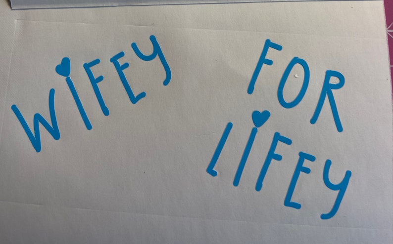 May include: A white card with the words "WIFEY FOR LIFEY" written in blue with a small blue heart above each word.