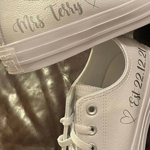 May include: White leather sneakers with a heart and the text "Mrs Terry" on one shoe and a heart and the text "Est 22.12.21" on the other shoe.
