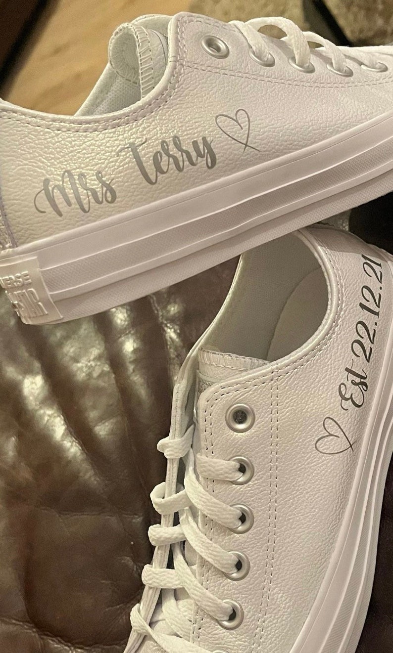 May include: White leather sneakers with a heart and the text "Mrs Terry" on one shoe and a heart and the text "Est 22.12.21" on the other shoe.