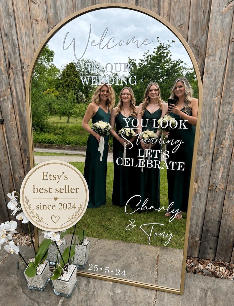 May include: An arched floor mirror with a gold frame featuring white text that reads Welcome TO OUR WEDDING, YOU LOOK stunning LET'S CELEBRATE, Charly & Tony, and 25.5.24. A circular sign reads Etsy's best seller since 2024 with white orchid plants.