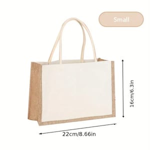 Puede incluir: Una bolsa de tela blanca pequeña con ribete y asas de yute marrón. La bolsa mide 22 cm de ancho y 16 cm de alto. "Small" está escrito en un óvalo beige.