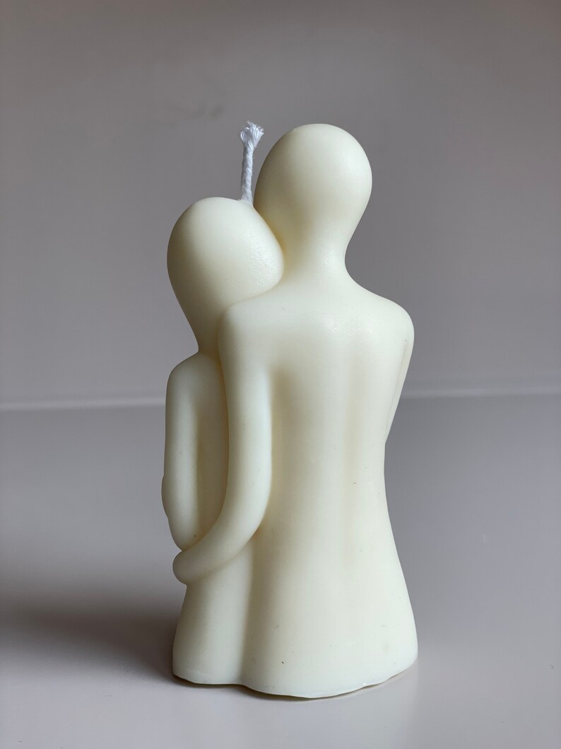 May include: A white candle sculpted in the shape of two figures embracing. The candle has a single wick.