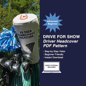 May include: A grey golf club headcover with a horseshoe and flag design, the text "JB 2026 Tournament Champion", and a black tornado graphic. The headcover is on a golf club with a blue and white pom-pom.