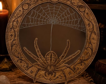 May include: A circular wooden mirror frame featuring an intricate laser-engraved spider and web design. The border is decorated with etched celestial moon phases and vine patterns. The spider is positioned at the bottom, with a web extending upward.