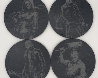 May include: Set of four round black slate coasters. Each coaster features a detailed etched image of a horror movie character with a hockey mask, holding various weapons. The coasters are a dark gray color.