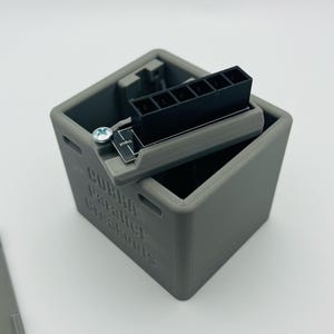 May include: A gray 3D printed box with the words "CUBED Parallel Breakout" printed on the side. The box is open and a black connector with six pins is visible inside.