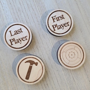 May include: Four wooden game pieces with different designs. One piece says "First Player", another says "Last Player", a third has a hammer design, and the last piece has a target design.