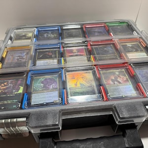 May include: A gray plastic storage case filled with various trading cards. The cards are in individual clear plastic holders, with blue and red accents. The case has a black handle and latches, and is partially open.