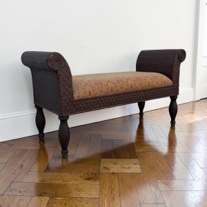 May include: A dark brown woven bench with scrolled arms and a rectangular seat cushion featuring a gold and brown damask pattern. The bench is supported by four dark brown turned wooden legs with a smooth, polished finish and rounded feet.