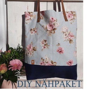 Könnte beinhalten: Eine hellblaue Tragetasche mit Blumenmuster und braunen Lederriemen. Die Tasche hat einen dunkelblauen Boden und einen kleinen herzförmigen Patch auf der Vorderseite. Der Text "DIY NÄHPAKET" ist unten im Bild gedruckt.
