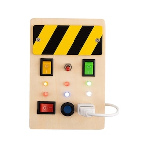 May include: A wooden control panel with a yellow and black striped warning sign, three toggle switches, a red button, a blue button, and six lights. The panel has a white cord with a USB connector.