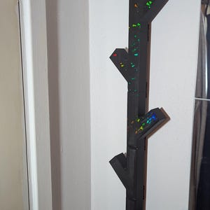 May include: A black wooden coat rack shaped like a tree branch with rainbow-coloured accents. The rack has four branches for hanging coats, hats, or scarves.