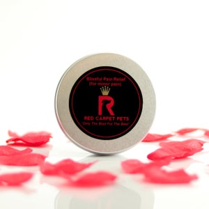 Peut inclure: Une boîte en étain argentée avec une étiquette noire qui indique "Blissful Pain Relief (for minor pain)" et présente un "R" rouge surmonté d'une couronne. L'étiquette indique également "RED CARPET PETS" et "Only The Best For The Best". La boîte est entourée de pétales de roses rouges.