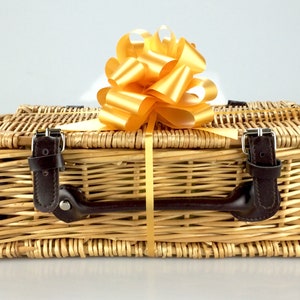 Puede incluir: Una cesta de mimbre con asa de cuero marr&oacute;n y lazo de cinta dorada. La cesta est&aacute; vac&iacute;a y lista para llenarse de regalos.