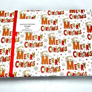 Puede incluir: Papel de regalo blanco con un patr&oacute;n repetido de texto "Feliz Navidad" en rojo y dorado con un peque&ntilde;o osito de peluche en cada "F".
