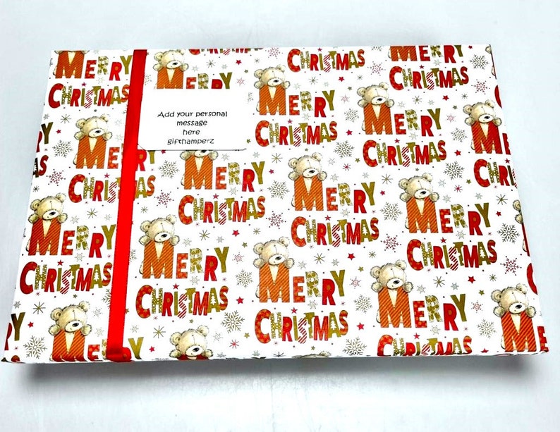 Puede incluir: Papel de regalo blanco con un patr&oacute;n repetido de texto "Feliz Navidad" en rojo y dorado con un peque&ntilde;o osito de peluche en cada "F".
