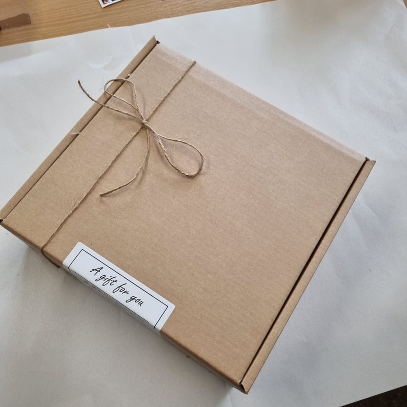 Puede incluir: Una caja de cart&oacute;n marr&oacute;n atada con cuerda y una etiqueta blanca que dice "A gift for you."
