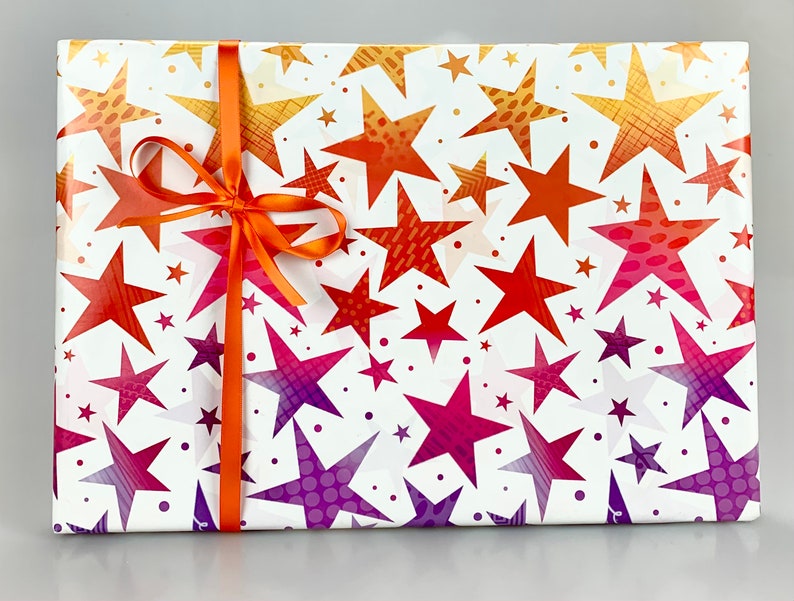 May include: A rectangular gift wrapped in white paper with a repeating pattern of stars in shades of orange, red, and purple. An orange ribbon is tied around the package in a bow. The stars have various textures and sizes.