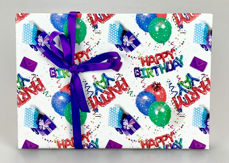 May include: A wrapped gift with a purple ribbon. The wrapping paper is white with a colorful birthday theme, featuring balloons, gift boxes, confetti, and the words "Happy Birthday" and "Party".