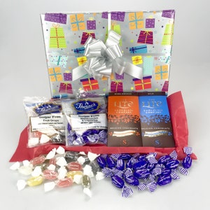 May include: A gift hamper wrapped in silver paper with colorful gift box designs and a silver bow. The hamper contains sugar-free sweets, Belgian chocolate bars, and a red tissue paper lining. A thoughtful gift for any occasion.