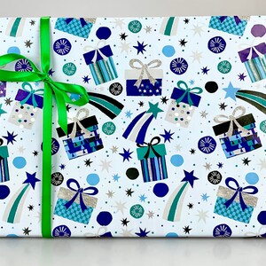 May include: A wrapped gift box with white wrapping paper featuring a pattern of blue and teal gift boxes, shooting stars, and starbursts. A bright green ribbon is tied around the box.