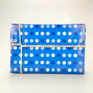 May include: A rectangular gift wrapped in blue paper with a polka dot pattern in shades of blue, silver, and white. The gift is tied with natural twine.