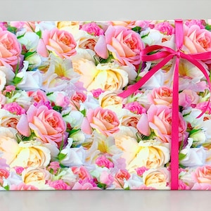 Puede incluir: Papel de regalo floral rosa y blanco con una cinta de raso rosa atada en un lazo.