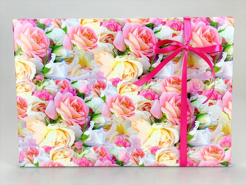 Puede incluir: Papel de regalo floral rosa y blanco con una cinta de raso rosa atada en un lazo.
