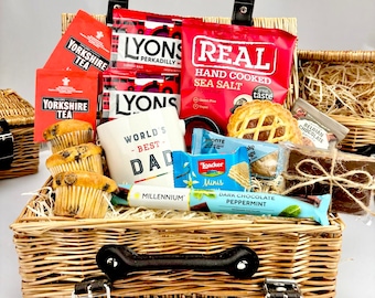 May include: A wicker gift basket containing Yorkshire Tea bags, Lyons coffee bags, Real sea salt potato chips, a white mug with World's Best Dad text, three blueberry muffins, a Bronte biscuit, Loacker Minis, and a Millennium chocolate bar.