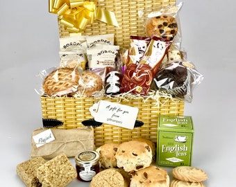 Può includere: Un cesto di vimini pieno di una varietà di leccornie, tra cui biscotti, scone, tè e un vasetto di marmellata. Il cesto è decorato con un fiocco giallo e un'etichetta regalo che recita "Un regalo per te da githamperz".