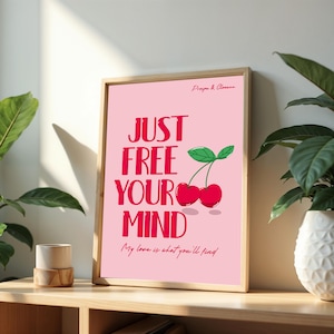 Puede incluir: Una impresión artística rosa enmarcada con las palabras "JUST FREE YOUR MIND" en letras rojas en negrita. Debajo del texto está la frase "My love is what you'll find" en una fuente cursiva. La impresión presenta una ilustración de cerezas.