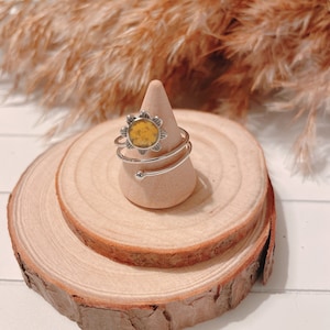 May include: A silver ring with a yellow flower design. The ring is on a wooden ring holder.