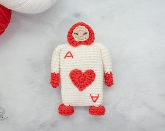 May include: A crocheted plush toy shaped like the Ace of Hearts playing card. The toy is white with red accents and has a heart-shaped face with closed eyes.