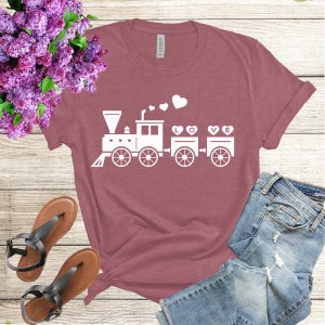 May include: A mauve t-shirt with a white graphic of a train carrying hearts that spell out "LOVE".