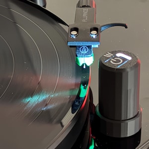 Puede incluir: Primer plano de un tocadiscos negro reproduciendo un disco de vinilo. La aguja, con la marca "Fluance", está en contacto con el disco. Un botón negro con un símbolo de encendido está visible.