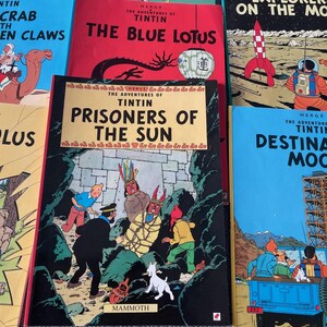 Peut inclure: Plusieurs bandes dessin&eacute;es Tintin, avec des couvertures color&eacute;es. On distingue des titres comme "Le Lotus Bleu" et "Les Sept Boules de Cristal". L'image pr&eacute;sente une pile de livres, mettant en valeur les illustrations classiques et le logo "MAMMOTH".