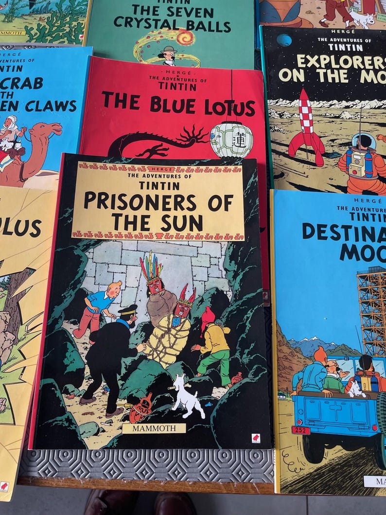 Peut inclure: Plusieurs bandes dessin&eacute;es Tintin, avec des couvertures color&eacute;es. On distingue des titres comme "Le Lotus Bleu" et "Les Sept Boules de Cristal". L'image pr&eacute;sente une pile de livres, mettant en valeur les illustrations classiques et le logo "MAMMOTH".