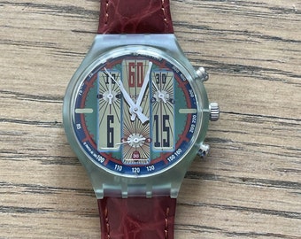 May include: A clear plastic wristwatch with a red leather band. The watch face has a multi-colored design with the numbers 60, 30, 15, and 6 printed on it.