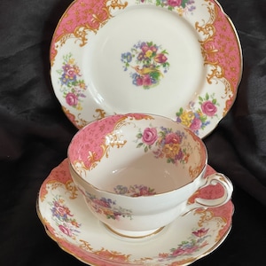 May include: A pink and gold teacup and saucer set with floral designs. The teacup has a delicate floral pattern and a gold rim. The saucer has a matching floral pattern and a gold rim.