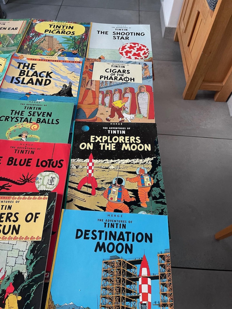 Peut inclure: Une collection de bandes dessin&eacute;es Tintin vintage, avec des couvertures color&eacute;es portant des titres tels que "L'&Eacute;toile Myst&eacute;rieuse", "On a march&eacute; sur la Lune" et "Objectif Lune". Les livres sont empil&eacute;s, pr&eacute;sentant diverses aventures du personnage embl&eacute;matique.