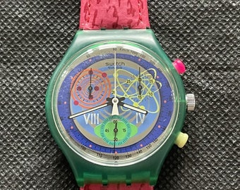 May include: A green and blue Swatch chronograph watch with a red and yellow patterned face. The watch has a red leather strap with a textured pattern.