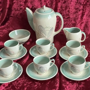 Puede incluir: Un juego de té vintage con un diseño floral verde y blanco. El juego incluye una tetera, una jarra de crema, un azucarero y seis tazas de té y platillos.