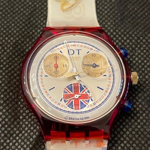 Puede incluir: Un reloj Swatch rojo y blanco con una esfera de cronógrafo. El reloj tiene un diseño de Union Jack en la esfera y el texto "Swatch AG 1995" en la parte inferior.