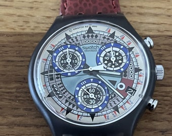 May include: A black Swatch chronograph watch with a patterned face and three sub-dials. The watch has a red leather band. The watch face features the text "SWATCH SWISS AG 1992".