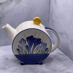 Könnte beinhalten: Eine weiße Teekanne aus Keramik mit einem blauen und weißen Blumendesign. Die Teekanne hat einen runden Körper und einen gelben Knopf auf dem Deckel. Die Teekanne steht auf einer weißen Oberfläche.